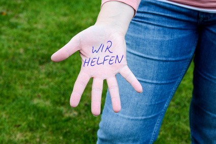Handinnenseite vor einem Bein, auf die mit Kugelschreiber Wir helfen gechrieben wurde