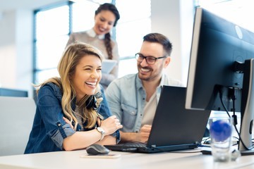 Lachende Frau und ein Mann sitzen an einem PC in einem Büro